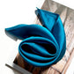 Kingfisher Blue silk scarf rolled on a book with natural light