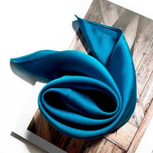 Kingfisher Blue silk scarf rolled on a book with natural light