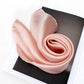 Rolled blush pink silk scarf displayed on book – satin sheen