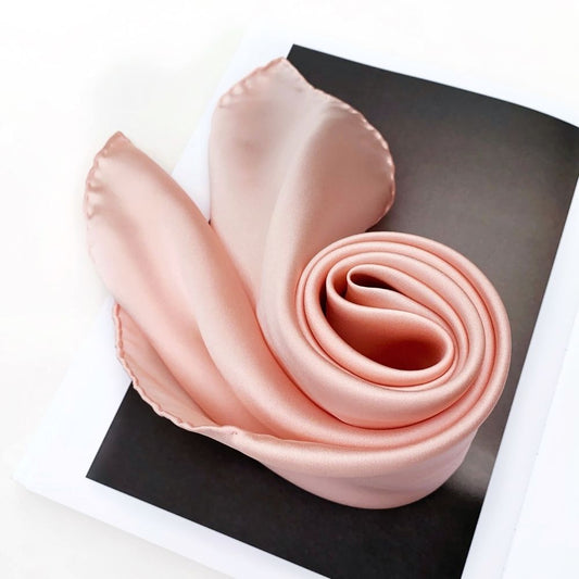Rolled blush pink silk scarf displayed on book – satin sheen