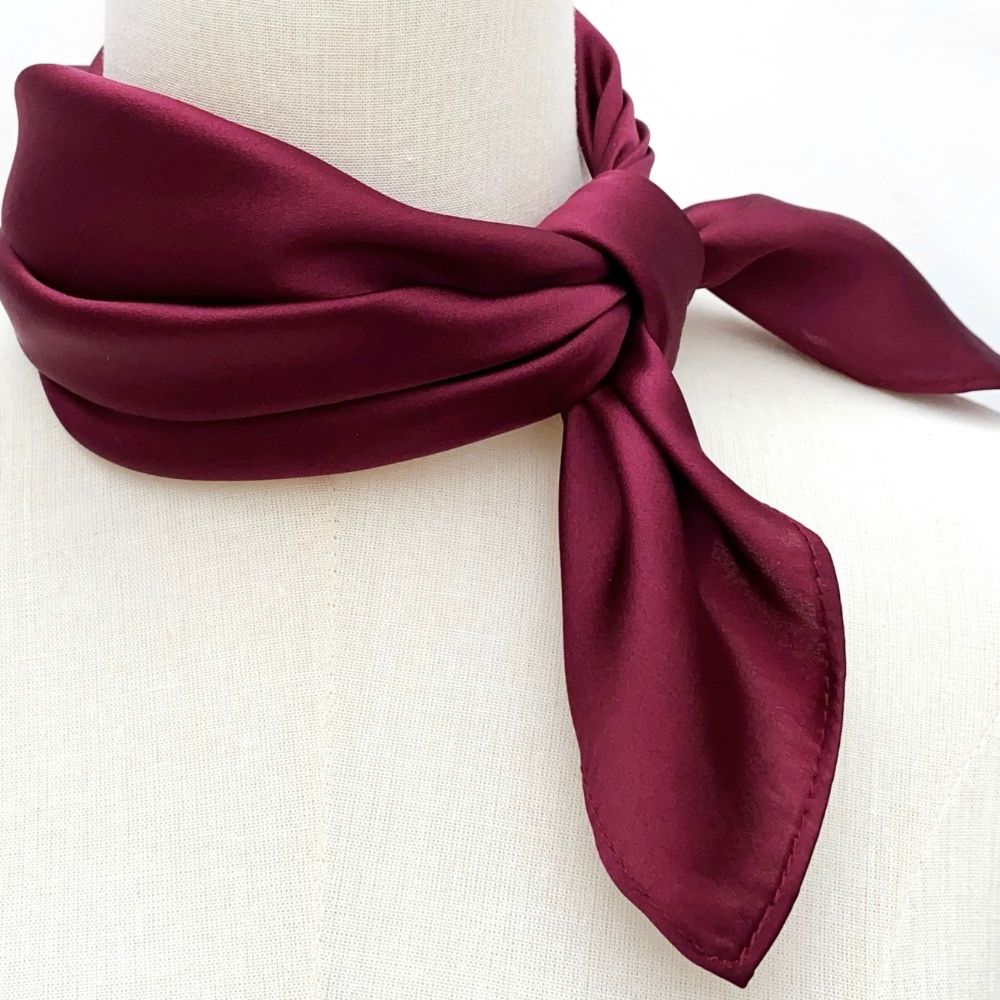 Burgundy silk scarf tied on a mannequin neck against a white background