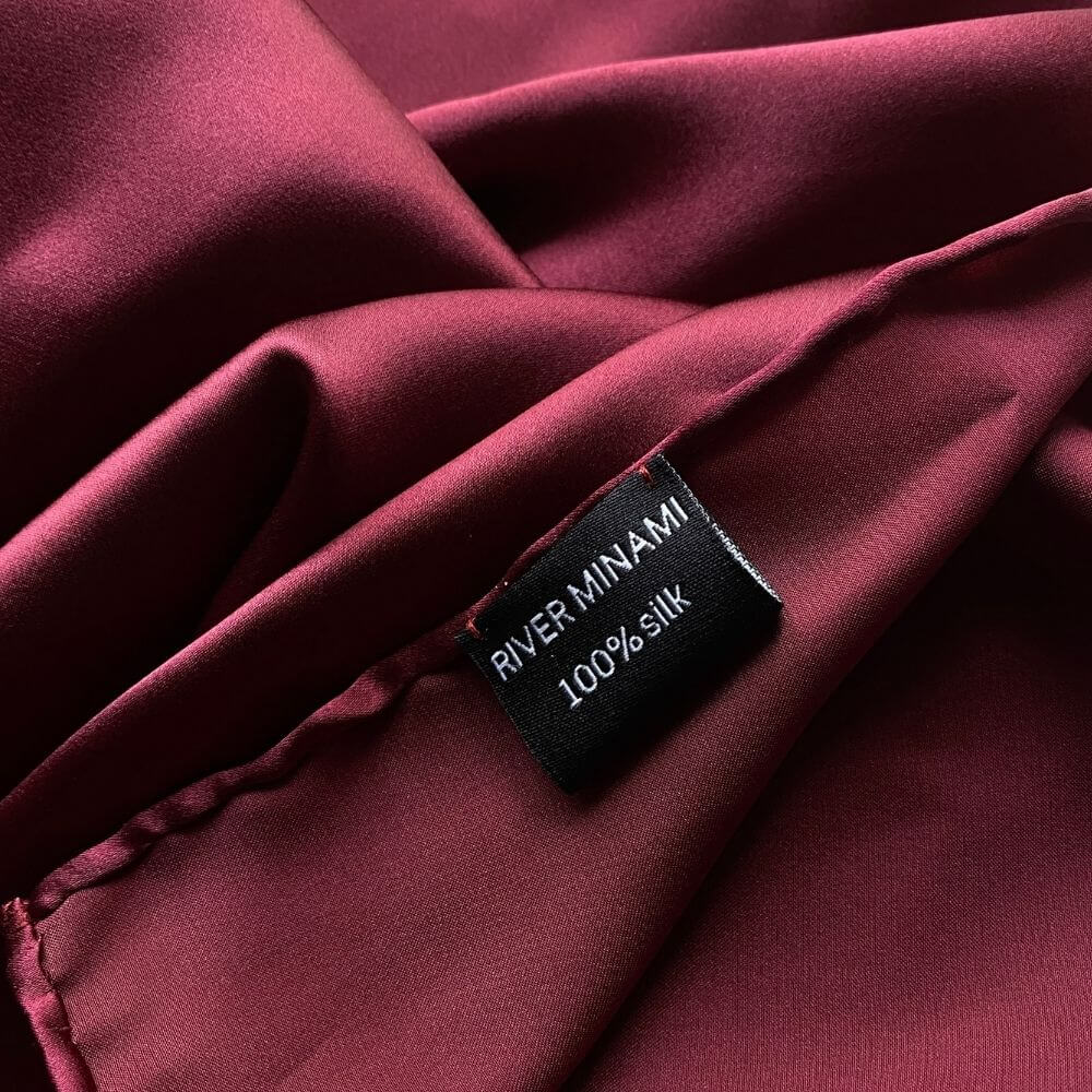Close-up of burgundy silk fabric with a 'RIVER MINAMI' and 100% silk washing label 