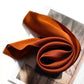 Burnt orange silk scarf rolled on book with warm autumn lighting