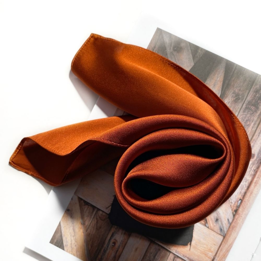 Burnt orange silk scarf rolled on book with warm autumn lighting