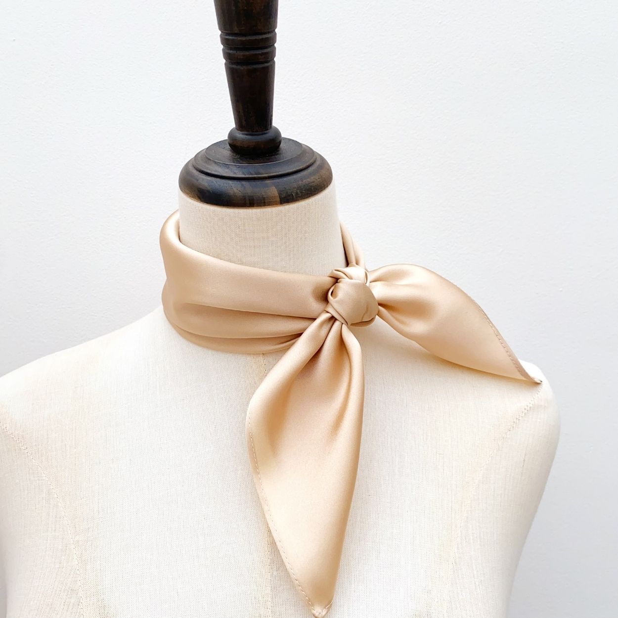 A champagne beige mulberry silk square neck scarf tied around a mannequin neck.