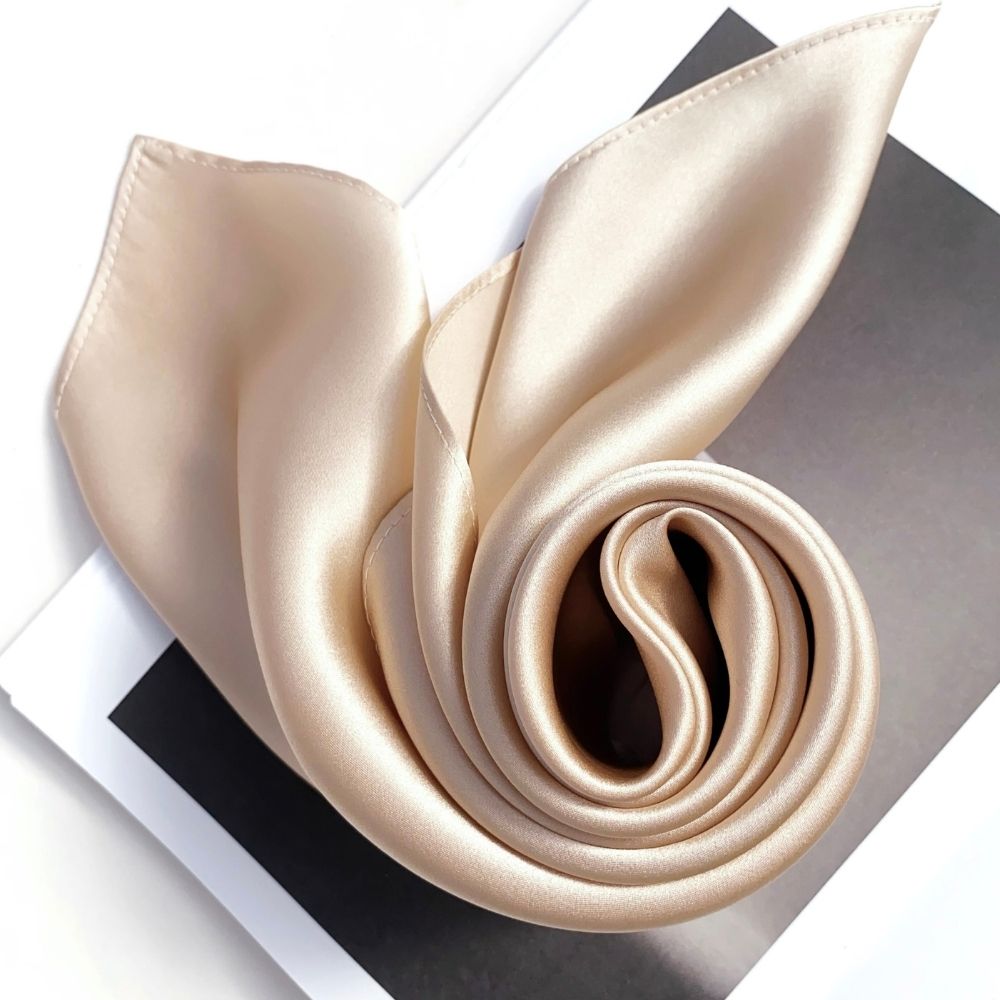 Rolled champagne beige mulberry silk scarf showing smooth satin texture on book