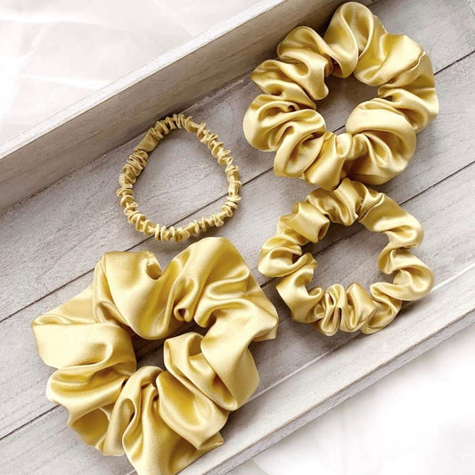 Set of soft yellow mulberry silk satin scrunchies on a wooden surface