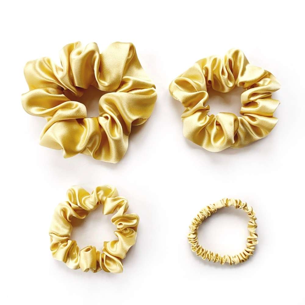 Four soft yellow gold mulberry silk satin scrunchies on a white background