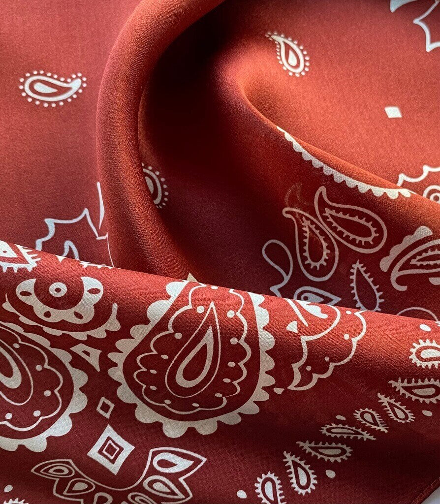 close up of a brick red mulberry silk scarf with white paisley patterns