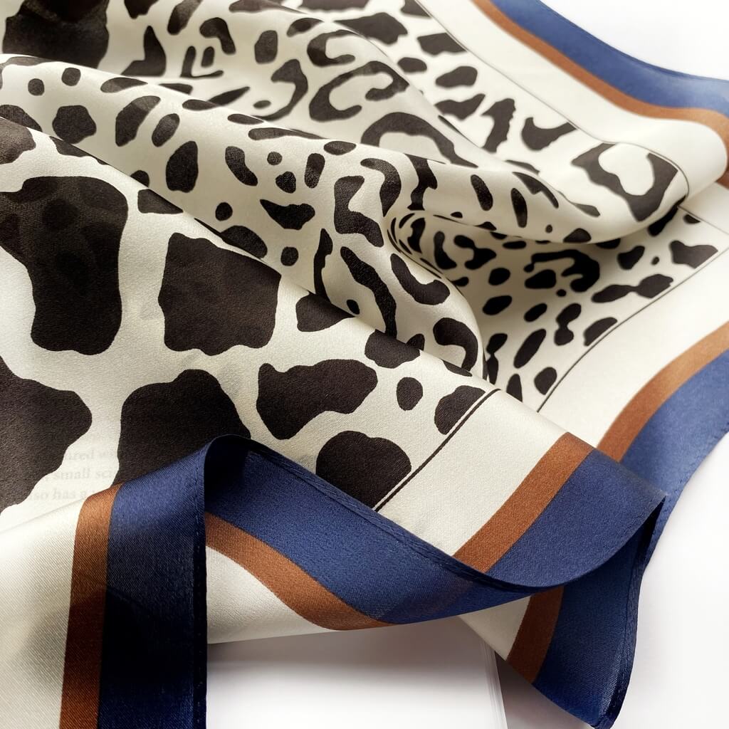 close up of a mulberry silk bandana scarf with black leopard print on ivory background and blue brown border on a white background