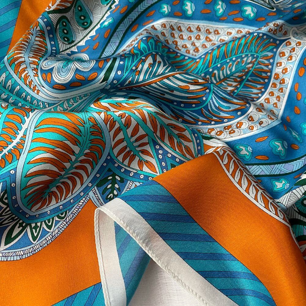 Close-up of a colorful mulberry silk square scarf with orange, blue, and white paisley patterns.