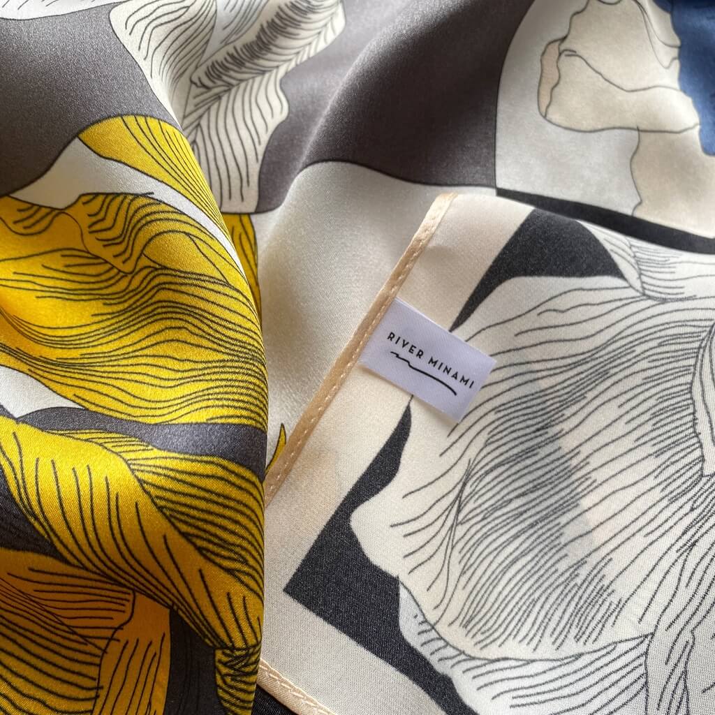 Close-up of a mulberry silk square scarf with artistic design and a visible "river minami" brand label.