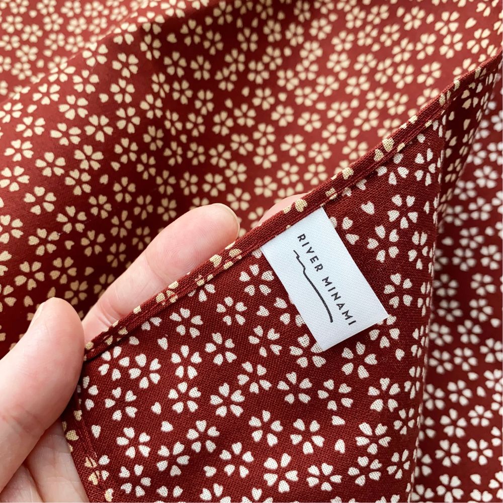 Red Japanese cotton square bandana scarf with cherry blossom floral pattern held by a hand, featuring a 'River Minami' label.