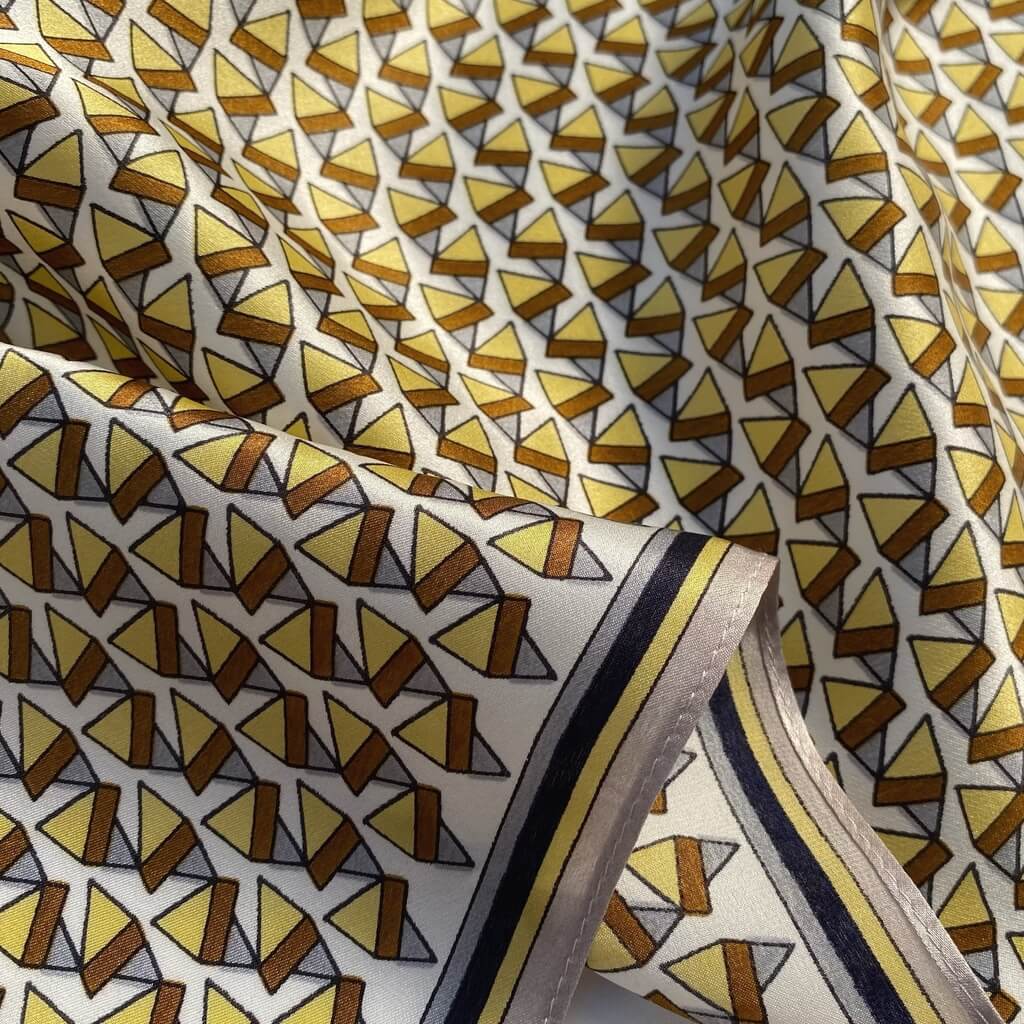 Close-up of mulberry silk bandana with a geometric triangle pattern in brown and yellow on a white background.