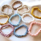 collection of assorted pastel and neutral mulberry silk skinny scrunchies hair ties laid out on a soft fabric background.