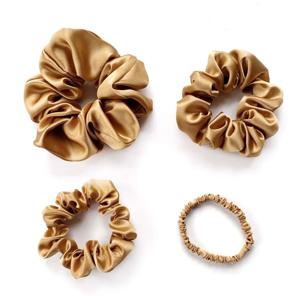 Four gold brown silk scrunchies of different sizes on a white background