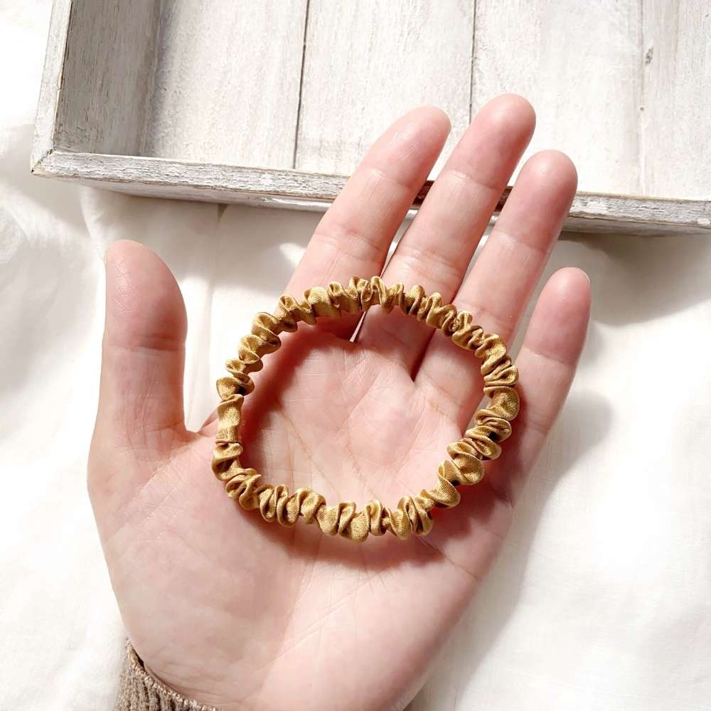 copper brown mulberry silk hair tie on a hand with a light wooden frame in the background