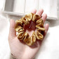 copper brown mulberry silk scrunchie held in a hand with a white background