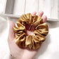 Medium copper brown mulberry silk scrunchie held in a hand with a light background