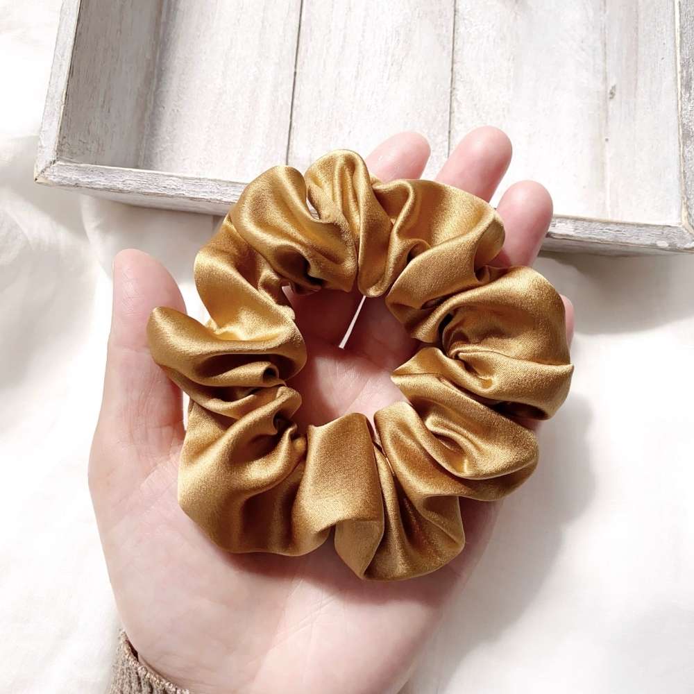 Medium copper brown mulberry silk scrunchie held in a hand with a light background