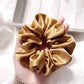 Large copper brown mulberry silk scrunchie held in a hand against a light background