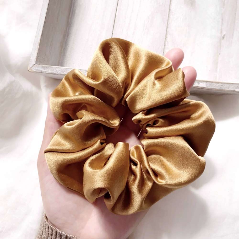 Large copper brown mulberry silk scrunchie held in a hand against a light background