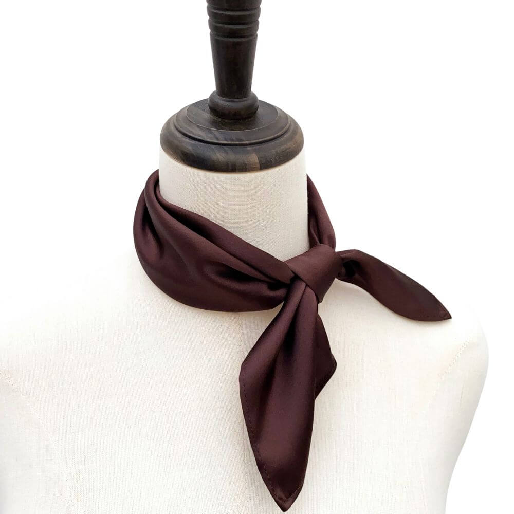 Brown silk scarf tied around a mannequin neck on a white background