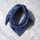 A mulberry silk square scarf in denim blue with a layered geometric, crosshatch, and paisley-inspired design placed on a light grey background.