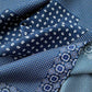 A close-up of a folded mulberry silk scarf in multiple blue patterns, including white paisley-like motifs and geometric floral designs on navy and light blue backgrounds.