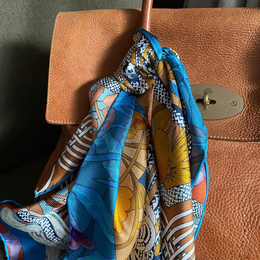 Colorful patterned mulberry silk twill square scarf draped over a brown leather handbag.
