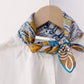 Colorful patterned mulberry silk square neck scarf tied around a white shirt on a wooden hanger.