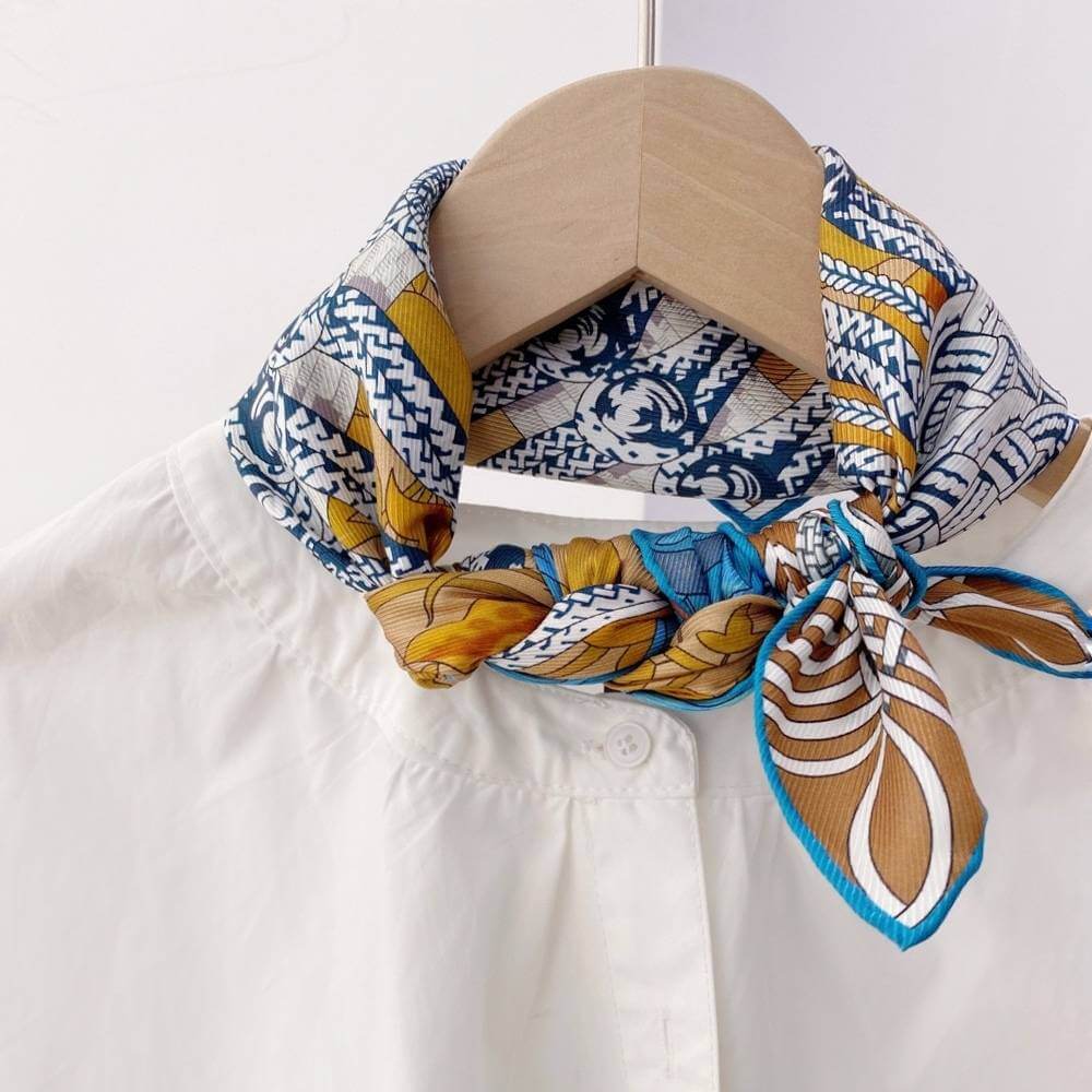 Colorful patterned mulberry silk square neck scarf tied around a white shirt on a wooden hanger.