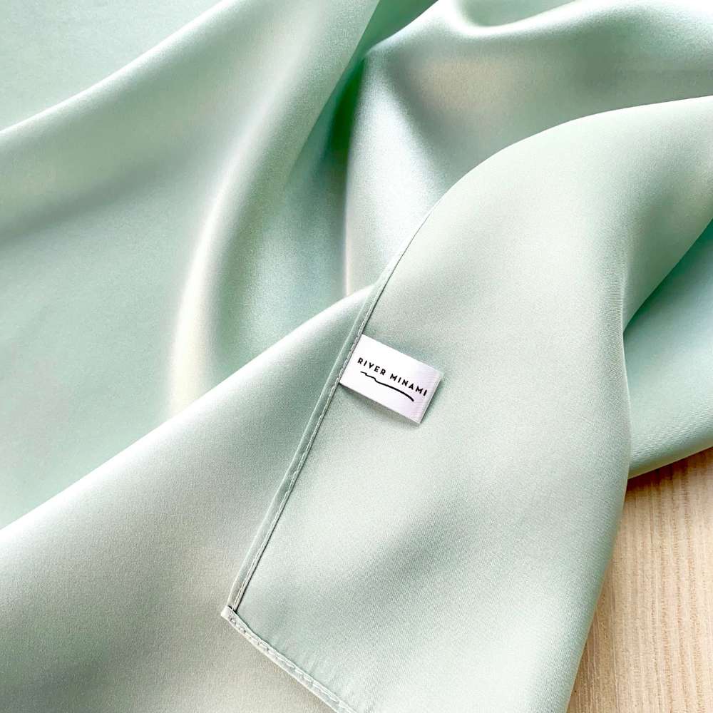 Light green silk scarf with a brand label on a wooden surface