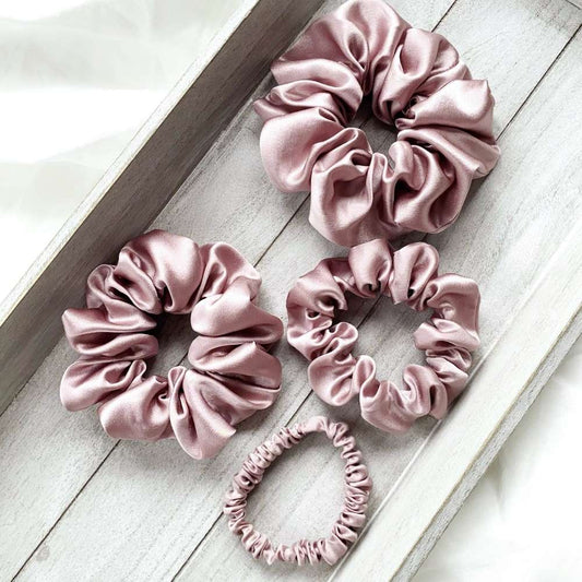 Set of pale mauve silk satin hair scrunchies on a light wooden surface