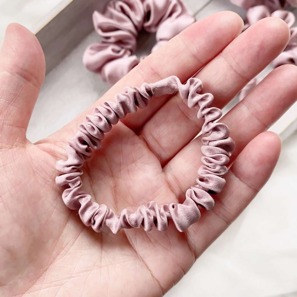 pale mauve silk satin hair tie on a hand with blurred pink scrunchies in the background