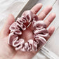 pale mauve silk satin hair scrunchie held in a hand with a light background