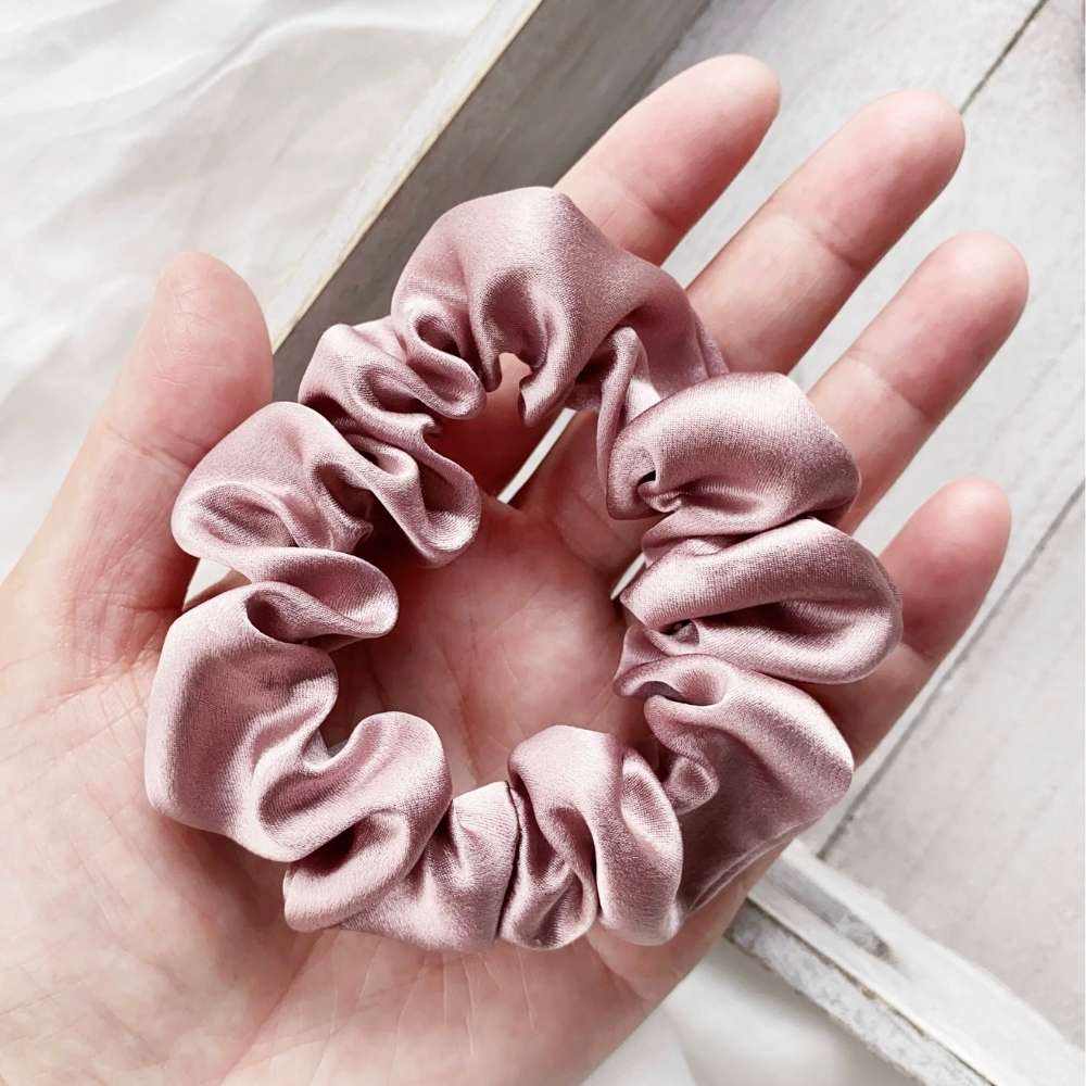 pale mauve silk satin hair scrunchie held in a hand with a light background