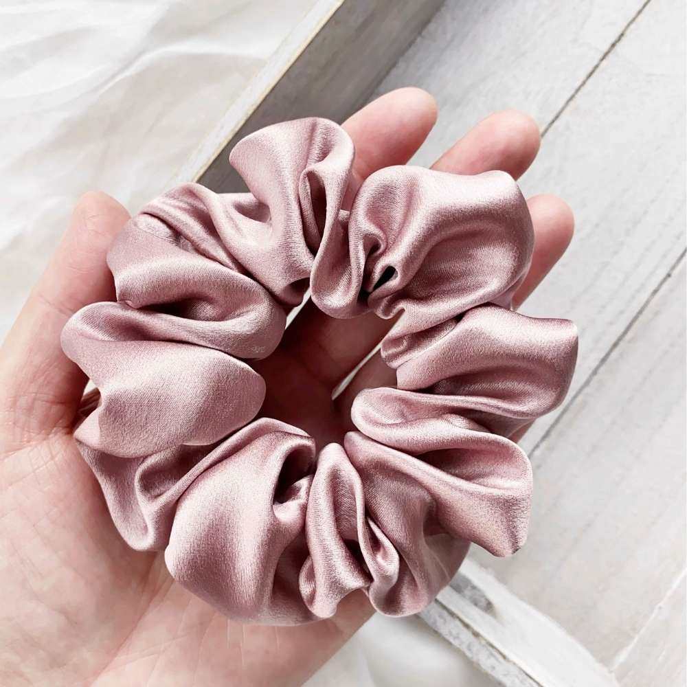 pale mauve silk satin hair scrunchie held in a hand on a light wooden surface