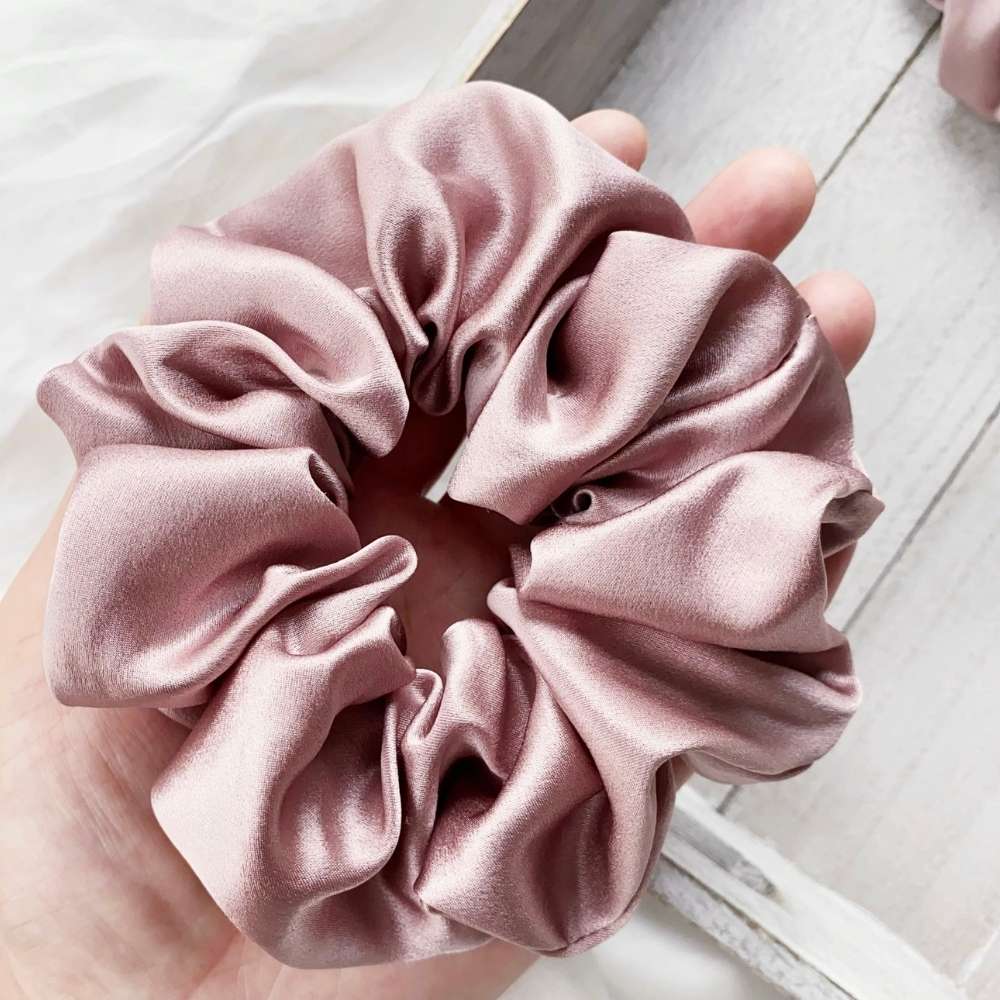 pale mauve silk satin hair scrunchie held in a hand on a light wooden surface