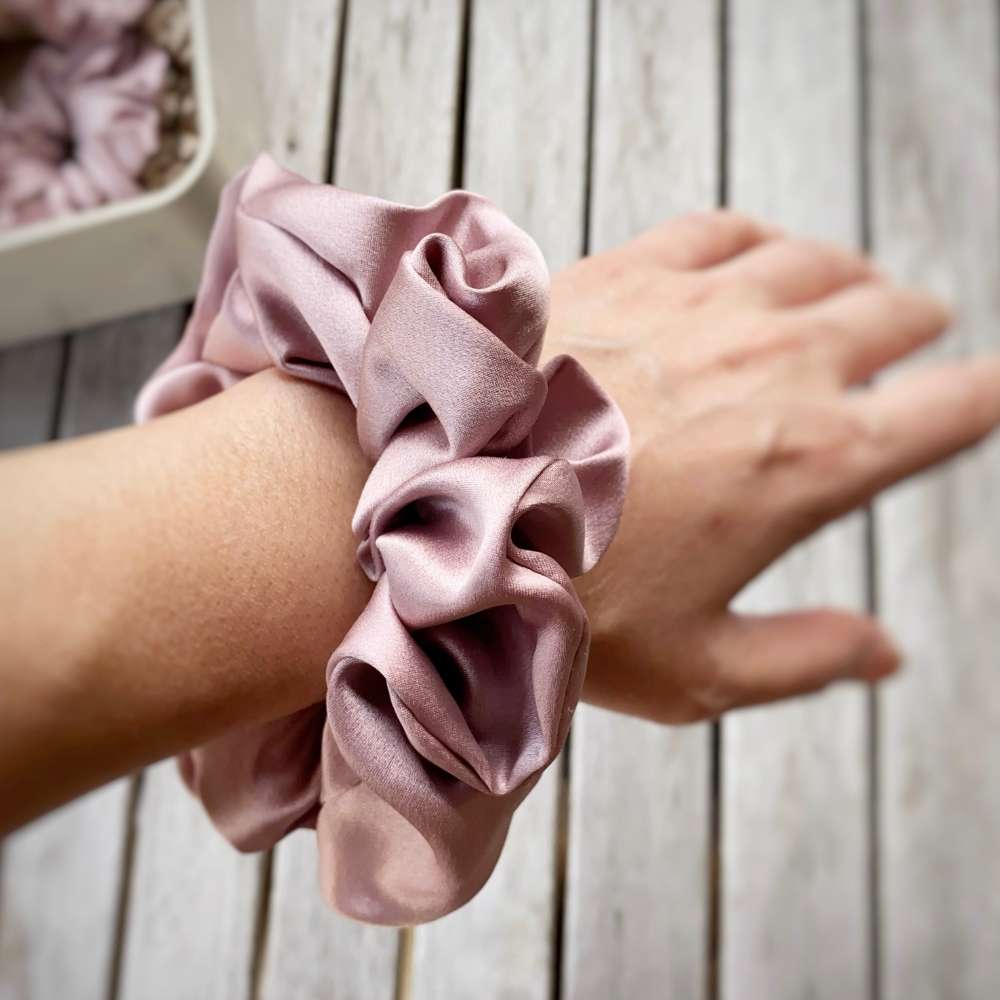 pale mauve silk satin hair scrunchie on a wrist with a wooden background