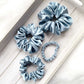 Four light blue mulberry silk scrunchies on a wooden surface
