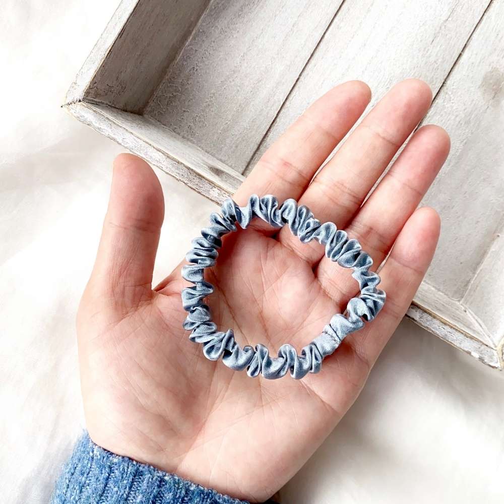 Hand holding a blue silk hair tie with a light wooden surface in the background