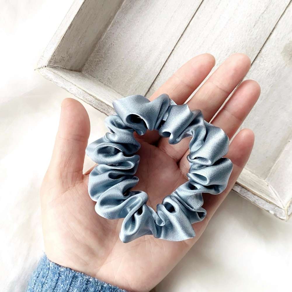Blue silk scrunchie held in a hand on a light wooden surface