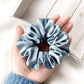 Light blue silk scrunchie held in a hand on a light wooden surface