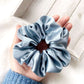 Blue silk scrunchie held in a hand with a light wooden background