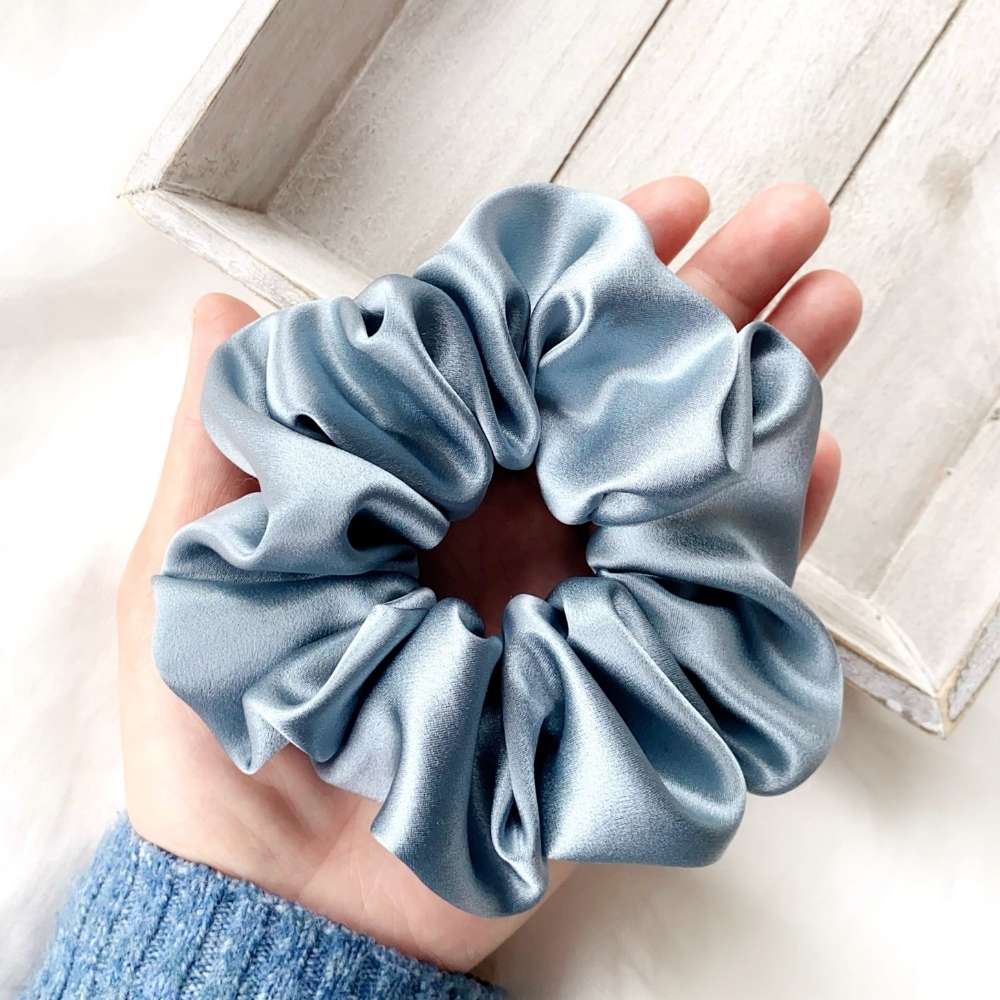 Blue silk scrunchie held in a hand with a light wooden background