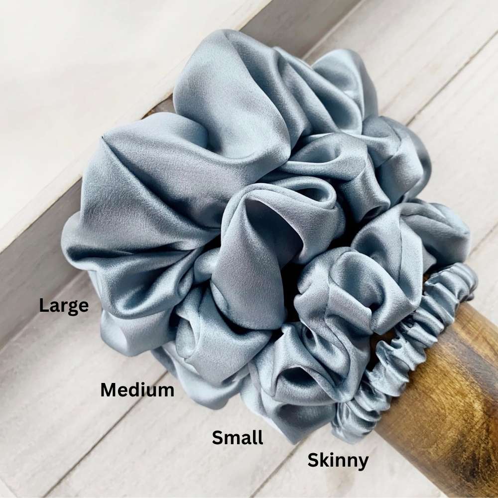 Set of four blue silk hair scrunchies labeled 'Large', 'Medium', 'Small', and 'Skinny' on a wooden surface.