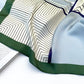 Close-up of a blue white geometric pattern mulberry silk square scarf with green edge on a white background.