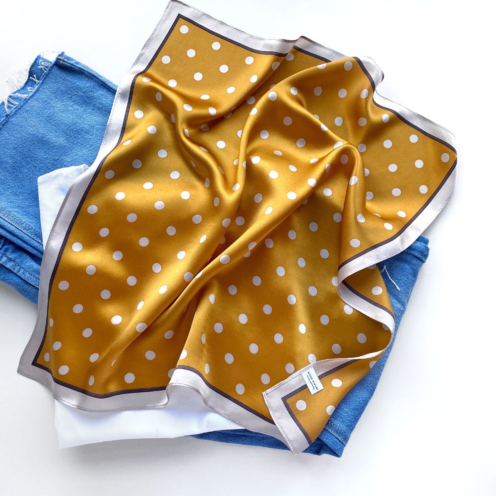 Flat mustard Yellow mulberry silk square scarf with beige cream polka dots print  on a blue jeans placed on the white background