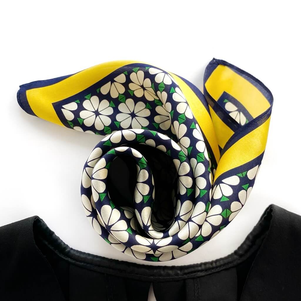 Folded floral patterned mulberry silk square scarf with yellow border on a white background